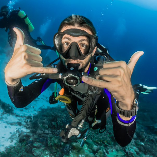 Enthusiastic young man scuba diving using shaka hand gestures